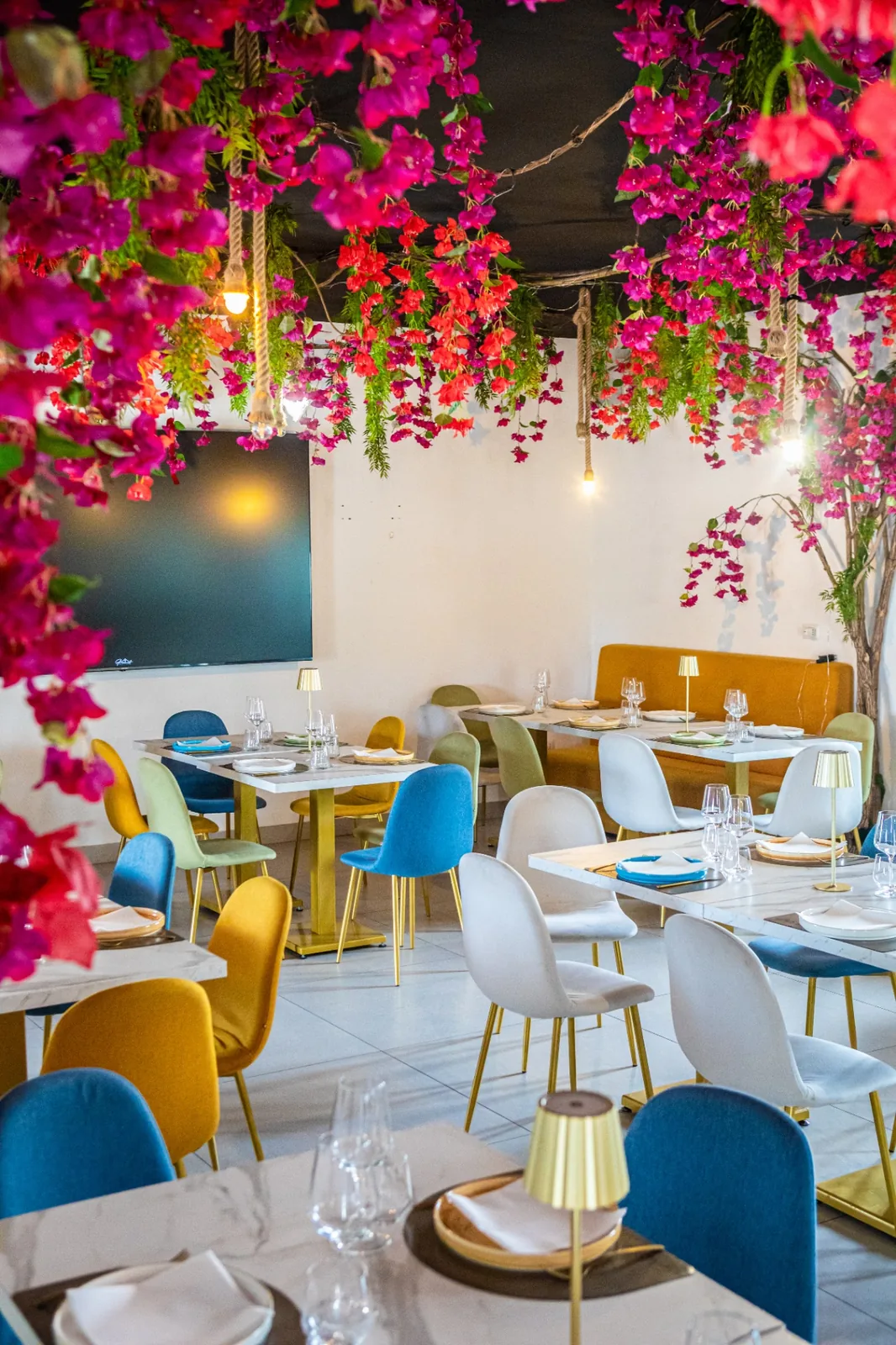 Sala colorata di A Casa Vost con tavoli in marmo e composizioni floreali sul soffitto