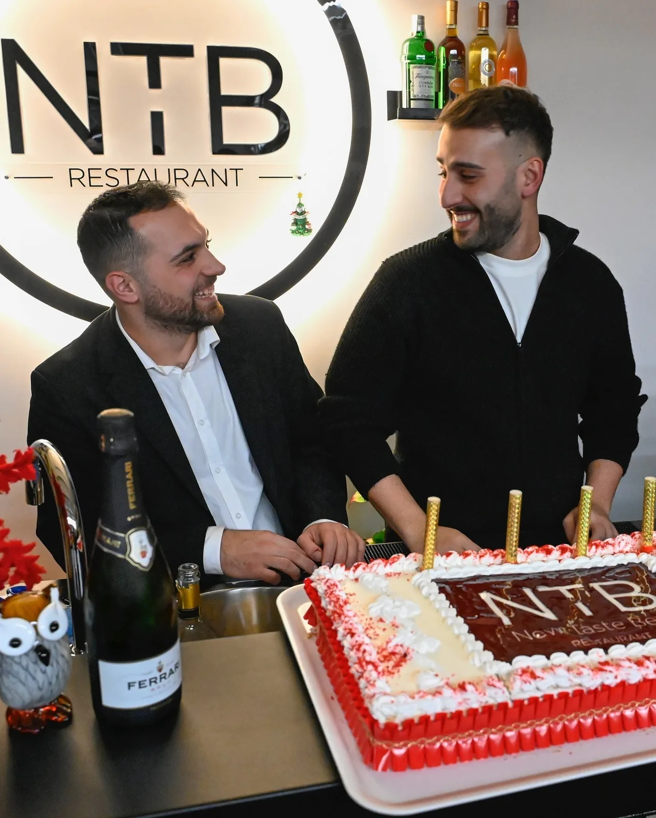 I due fondatori di N.T.B New Taste Beef davanti al logo del ristorante durante l'anniversario