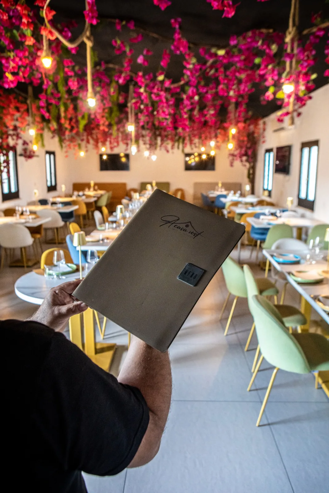 Menu di A Casa Vost presentato nella sala decorata con fiori e luci sospese