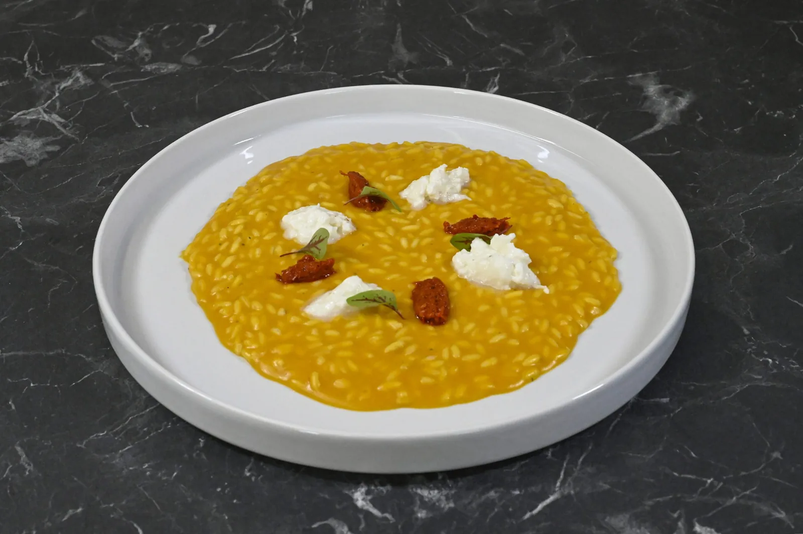 Risotto contemporaneo con crema gialla, formaggio fresco ed erbe servito da N.T.B